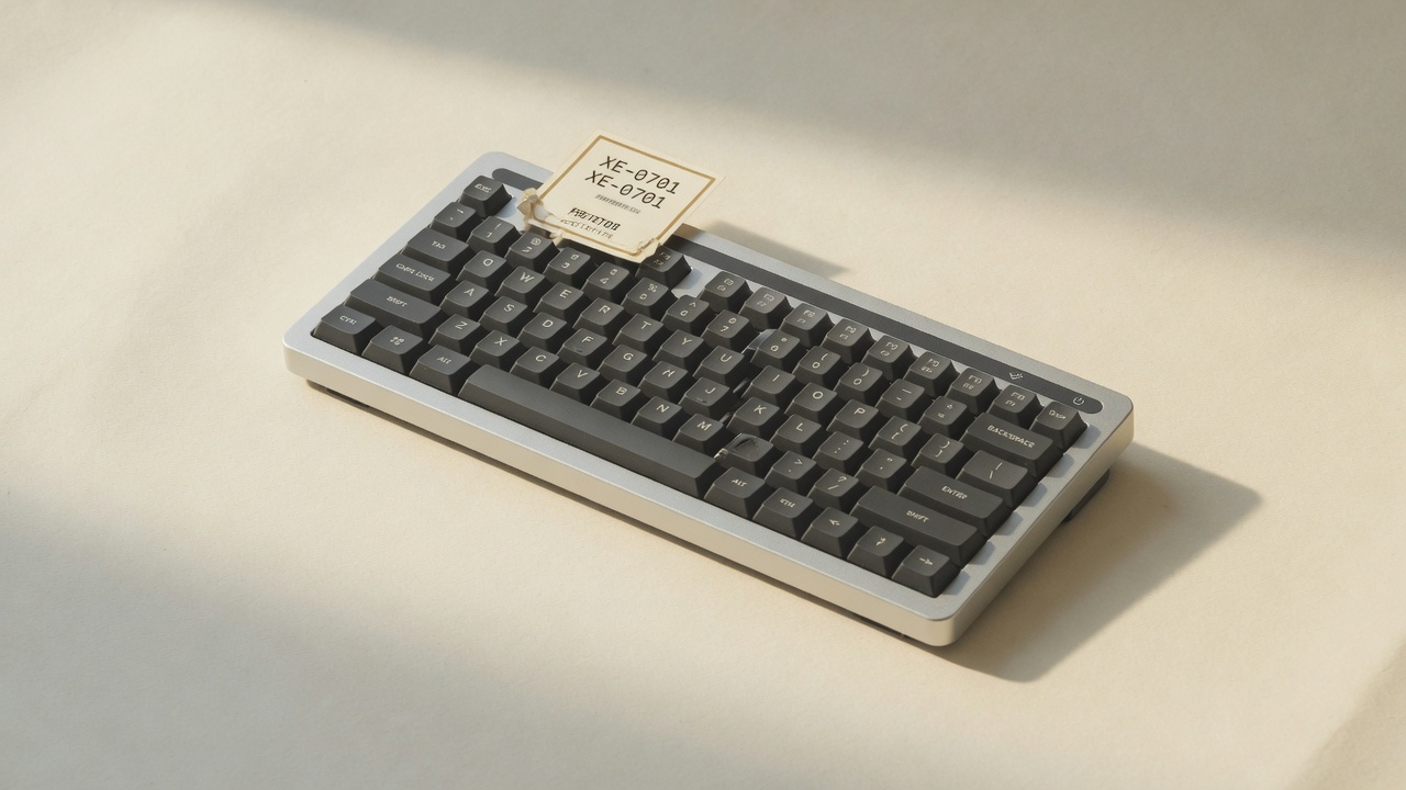 Charcoal keyboard with asset tag XE-0701 on a paper backdrop
