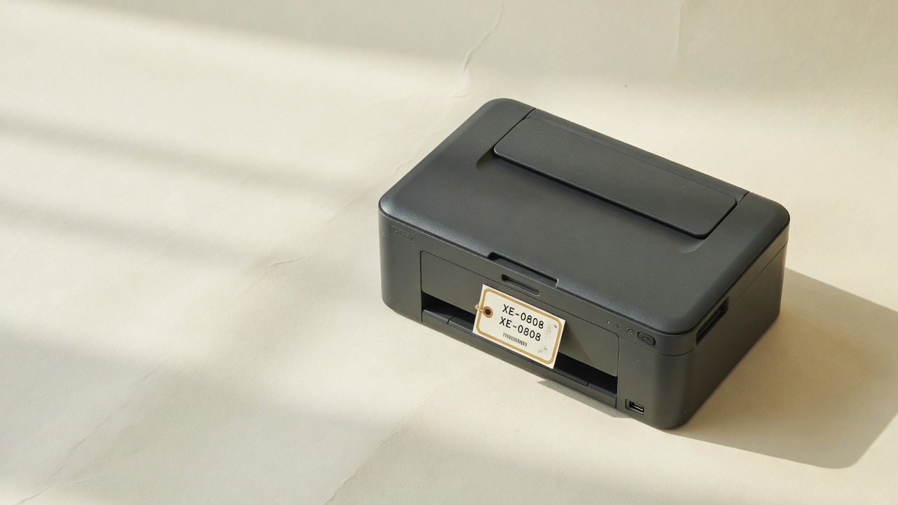 Desktop printer with asset tag XE-0808 on a paper backdrop