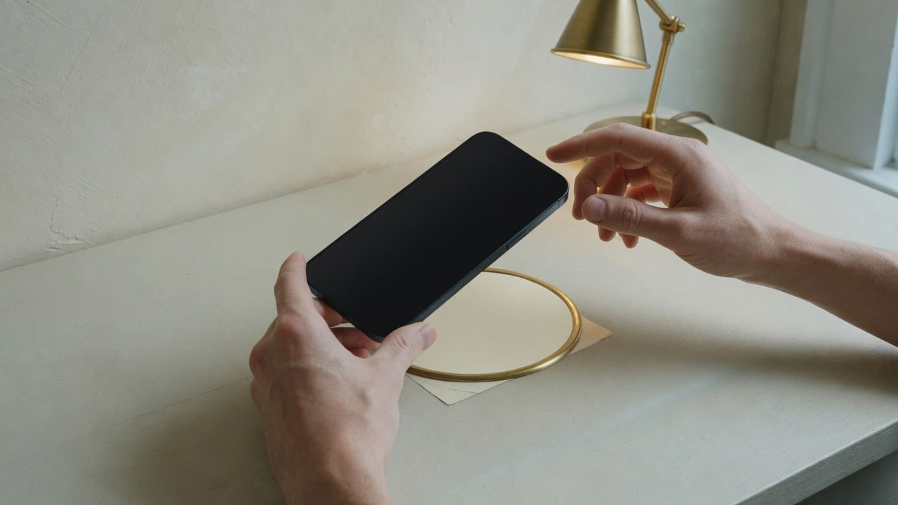 Hands holding a phone over a cream brass-rimmed label on a desk